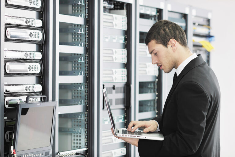Engineer using a laptop in a server room, monitoring Backup as a Service (BaaS) to ensure quick recovery and data protection.